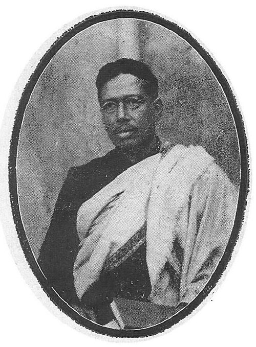 Half-length photographic portrait of Bipin Chandra Pal in spectacles, wearing a dark coat with a light shawl over one shoulder, reproduced within a printed oval frame.